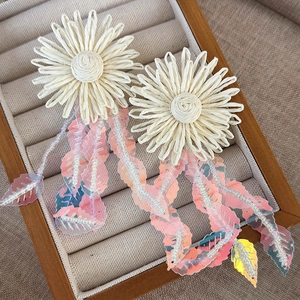 Detailed close-up of handmade woven sunflower earrings with shimmering pink petal sequins