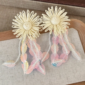 Macro detail of oversized woven straw sunflower earrings with pink leaf sequins and beads