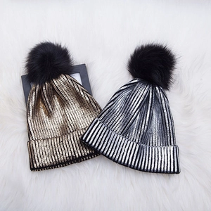 Detailed view of knitted pom-pom beanies in metallic gold and silver colors