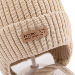 Detail of beige ribbed knit hat with leather patch featuring bear and Hand Made text