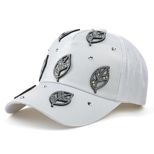 Close-up of white baseball cap featuring sparkling rhinestone leaf patches and silver studs