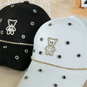 Detailed close-up of textured fabric with crystal bear and gold chain on baseball caps