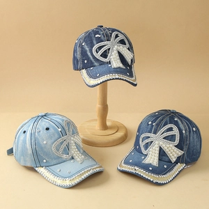Detailed view of denim baseball caps with luxury rhinestone bows and pearl embellishments