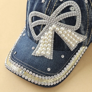 Detail of denim baseball cap featuring a pearl bow and sparkling rhinestone brim accents