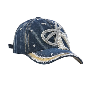 Blue denim baseball cap with a large rhinestone bow and pearl accents on white background