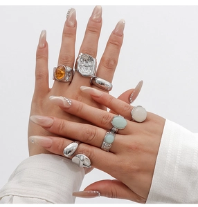 Close-up of stacked acrylic and alloy rings with amber and green stones on fingers