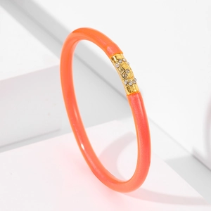 Detalle de una pulsera de gelatina naranja con dije de calavera dorada y cristales
