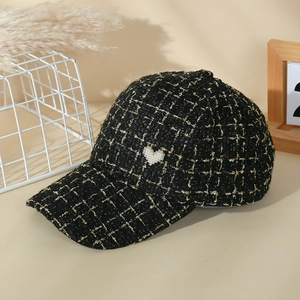 Detail shot of black tweed baseball cap featuring a white pearl heart embellishment