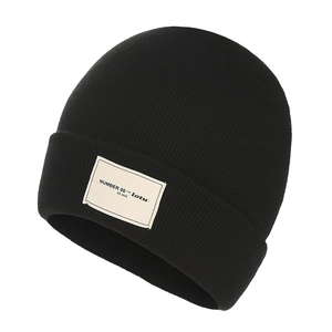 Minimalist black knitted beanie hat with white textile label and fine ribbed texture