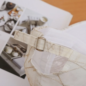Detailed macro view of the cream fabric texture and silver embroidered lines on the cap