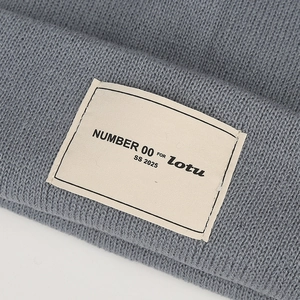 Close-up of grey knit beanie featuring a rectangular woven patch with brand lettering