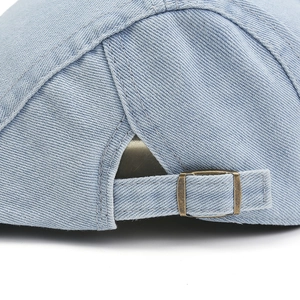 Detail view of denim beret with adjustable antique bronze buckle and stitching