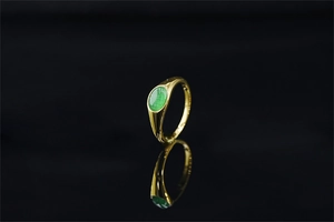 Dettaglio di un anello a sigillo dorato con una gemma verde ovale e finitura lucida