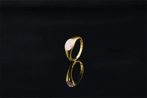 Dettaglio di un anello d'oro con una gemma rosa ovale su una superficie a specchio nera