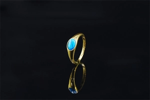 Dettaglio di un anello dorato con turchese ovale e incisione con texture verticale fine