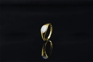 Macro di un anello a sigillo dorato con gemma ovale bianca su fondo nero con riflesso liscio