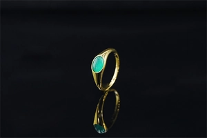 Dettaglio di un anello in oro lucido con una gemma verde ovale su sfondo nero profondo