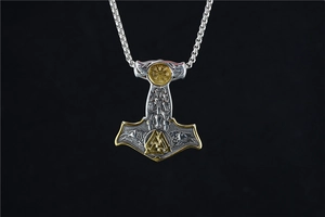 Vue macro du pendentif Mjölnir aux symboles vikings dorés et Valknut sur un fond noir uni