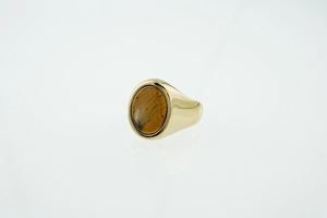 Detail of a polished gold signet ring featuring a natural oval tiger eye gemstone inlay