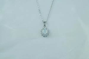 Macro shot of oval white opal pendant with sparkling zircon halo on light blue silk