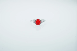 Macro detail of silver ring featuring oval red gemstone and side diamond accents