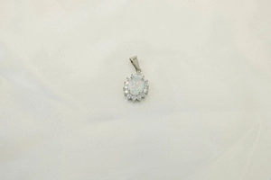 Detailed view of an oval opal pendant necklace with shimmering zircon accents on white fabric