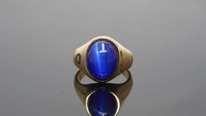 Macro shot of gold wide band ring with a large oval blue gemstone on a reflective surface