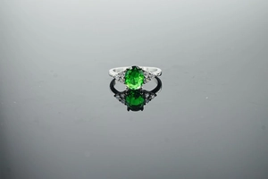 Close-up of oval green gemstone ring with side diamonds on polished silver band
