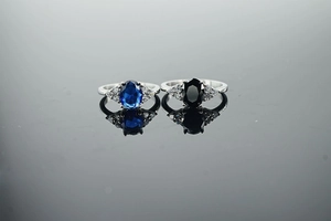 Detailed macro view of two silver rings with oval blue and black gemstones on a reflective base