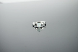 Detailed shot of ocean blue opal ring with silver steel band on dark mirror background
