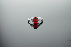 Detailed close-up of oval red gemstone ring with side stones on dark reflective surface