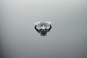 Close-up of silver ring with large oval gemstone and side cluster diamonds on dark mirror