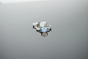 Macro shot of two silver rings with blue fire opals reflected on a dark grey surface