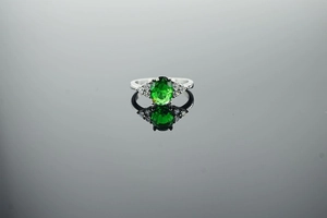 Macro shot of an oval green gemstone ring with white zircon side stones and reflection