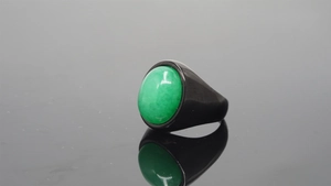 Macro detail of a vintage black band ring with an oval green gemstone on black mirror surface