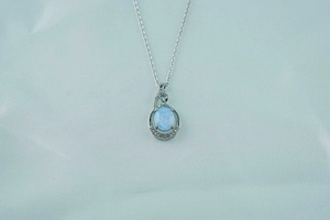 Macro detail of tear-drop opal pendant necklace in silver finish on blue silk background