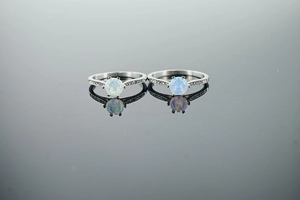 Detailed macro view of minimalist silver opal rings with side stones on a mirror surface