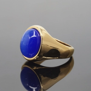 Polished gold ring with an oval blue cat-eye stone and thick metal band on a black surface