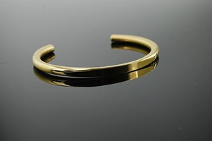 Macro shot of polished gold C-shape open bangle with reflective mirror surface