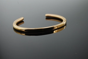 Detailed macro shot of the polished gold-plated C-shaped cuff bracelet with mirror reflection