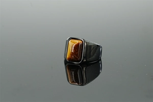 Macro shot of men's black titanium ring with rectangular tiger eye stone on mirror surface