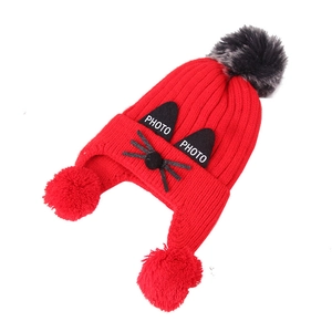 Detail of red knitted winter hat for kids with triple faux fur pom-poms and cat design