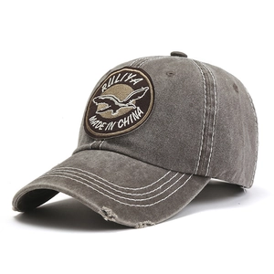 Macro shot of vintage washed grey baseball cap with embroidered flying bird patch and distressed detail