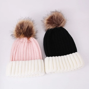 Detail of color-block knit beanies with fluffy faux fur pom-poms in pink and black