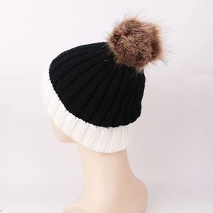 Close-up of black and white knit beanie with a fluffy brown faux fur pom-pom detail