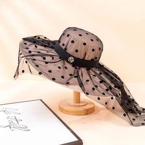 Chapeau de soleil à large bord avec tulle à pois noirs et ruban décoratif sur support élégant