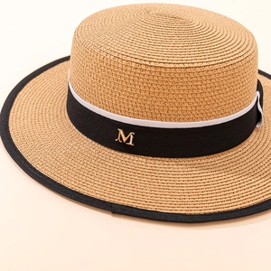 Detail of a natural boater straw hat with black ribbon edge and golden M metal logo