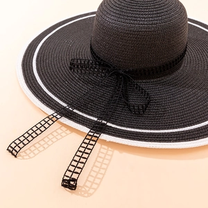 Detail of elegant black wide brim straw sun hat with white stripe and mesh bow tie