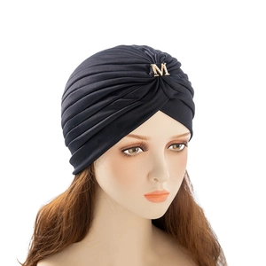 Detail of black pleated turban hat featuring a golden metal M buckle with small rhinestones