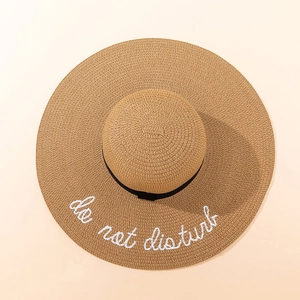 Detailed embroidery of do not disturb text on wide brim straw sun hat with black ribbon